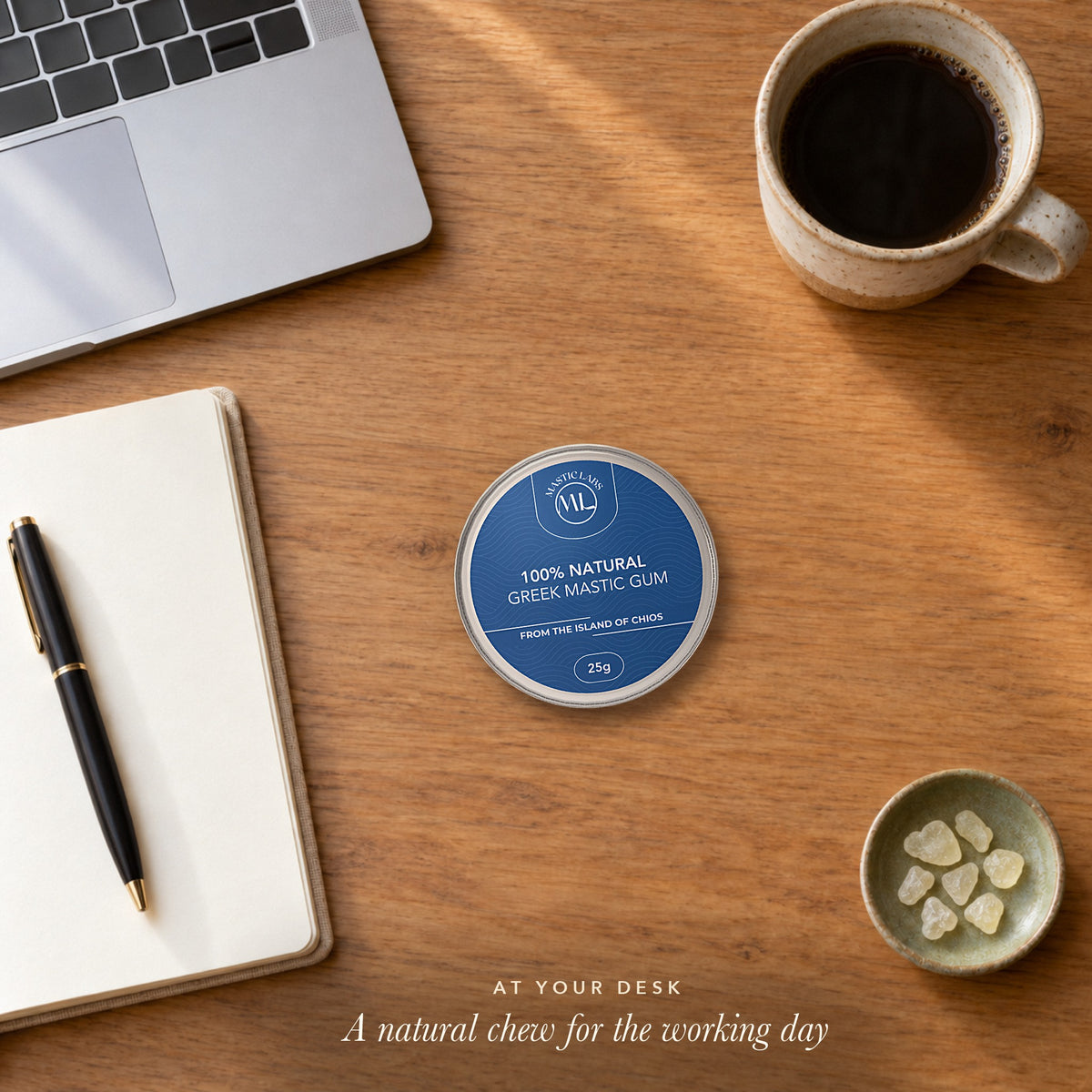 Tin of Greek mastic gum on a wooden desk beside a laptop, notebook, coffee and a small dish of mastic tears